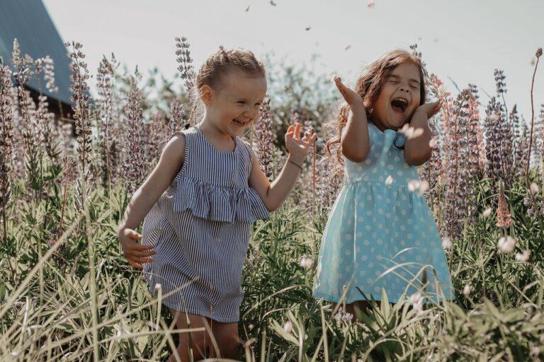 Deux jeunes enfants rient et s'amusent dans un champ de fleurs sauvages, illustrant la vision simple et authentique du monde à travers les yeux d'un enfant.